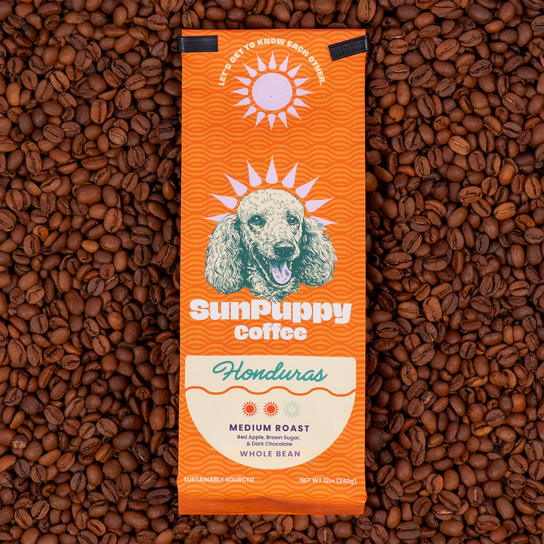 Sunpuppy Coffee Honduran medium roast whole bean coffee in orange packaging featuring golden retriever mascot with sun logo on pink background 12 ounces